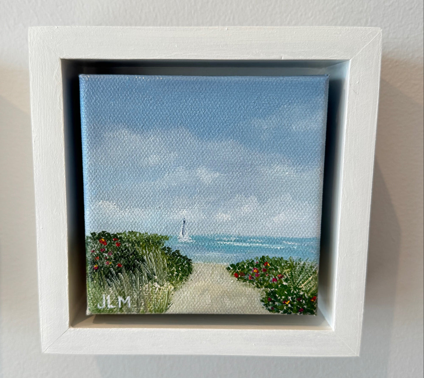 Framed artwork with a scenic view of water and plants on a white wall.